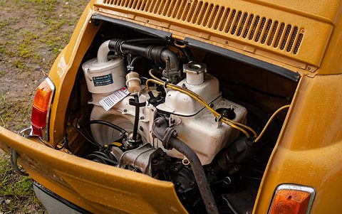 Rear engine bay of an ochre Fiat 500 with a white air filter, the twin-cylinder engine and yellow fuel lines. Opens a larger view