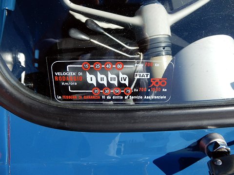 Black sticker with red circled numbers for each of four gears and the Fiat 500 logo, behind a blue steering wheel.
