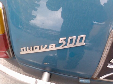 Chrome script reading nuova 500 on a blue engine lid, beside the edge of a red tail lamp. Opens a larger view