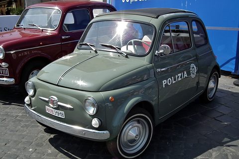 Grey-green Fiat 500 with a police plate and POLIZIA on the door, a maroon car and a blue banner behind. Opens a larger view