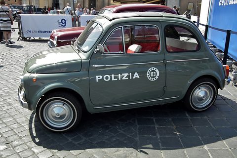 Grey-green Fiat 500 with POLIZIA and a 113 emblem on its door, on cobbles in sunshine. Opens a larger view