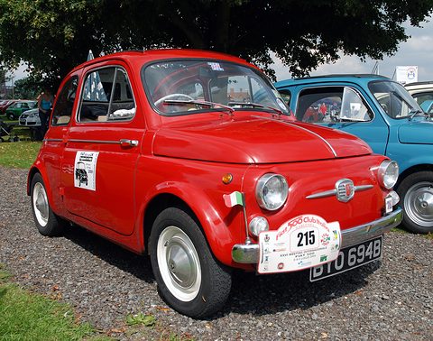 Red Fiat 500 with an Italian flag and a numbered rally plate on its bumper, parked on gravel beside a blue 500. Opens a larger view