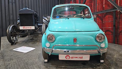 Front of a turquoise Fiat 500 with chrome bumper guards and a red badge, an old tractor beside it. Opens a larger view