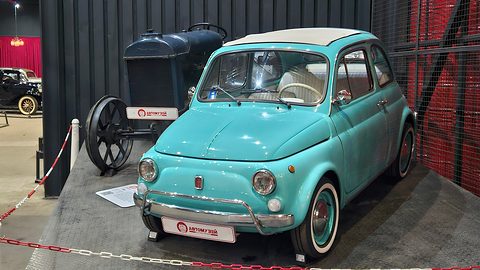 Turquoise Fiat 500 with a cream roof and whitewall tyres on a dark plinth beside an old tractor. Opens a larger view