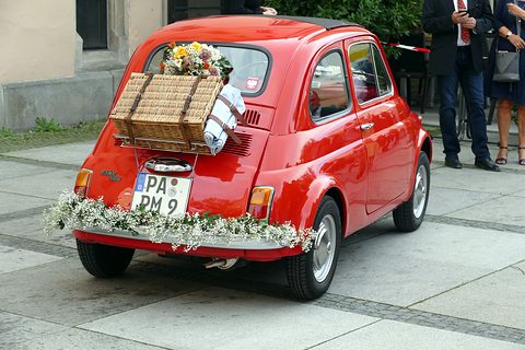 Red Fiat 500 from the rear with a wicker hamper and flowers on the engine lid and white garlands on the bumper. Opens a larger view