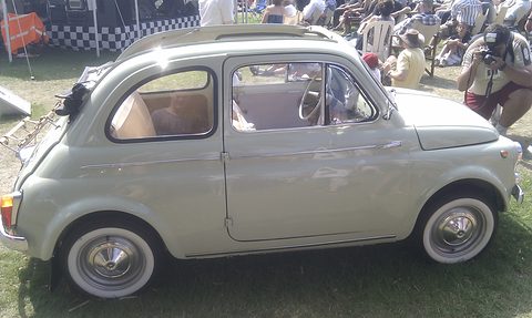 Side view of a pale grey Fiat 500 with whitewall tyres and a roof rack, spectators in deckchairs behind. Opens a larger view