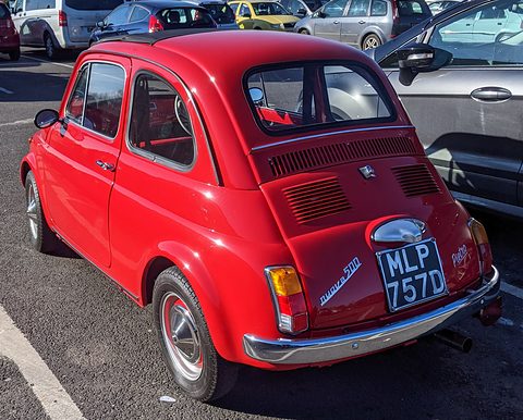 Red Fiat 500 from the rear right with nuova 500 script and a black British plate, in a car park. Opens a larger view