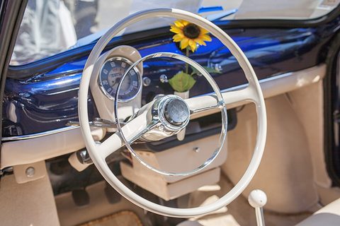 Blue painted dashboard with a round speedometer, a cream two-spoke steering wheel and a sunflower in a vase. Opens a larger view