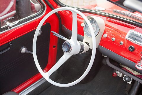 Red painted dashboard with a single round speedometer, a thin white two-spoke steering wheel and small switches. Opens a larger view