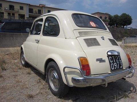 Cream Fiat 500 from the rear right with tubular bumper guards and a black Italian plate, on dry grass. Opens a larger view