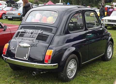 Black Fiat 500 from the rear left with a chrome rack on the engine lid and soft toys on the parcel shelf. Opens a larger view