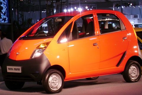 Bright orange small four-door hatchback with a black lower front and a Tata Nano plate, under show lights.