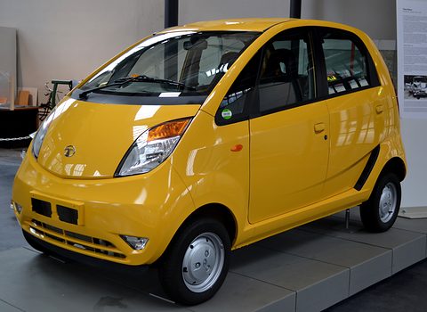 Bright yellow small hatchback on a grey museum plinth with information panels behind.