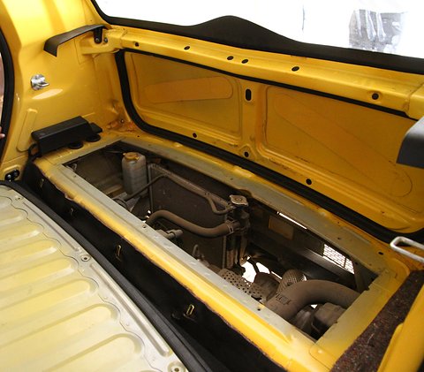 Yellow car interior with the rear floor panel lifted to show a small two-cylinder engine underneath.