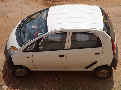 White small hatchback seen from a high angle, showing its roof and the length of its body, on red earth. Opens a larger view