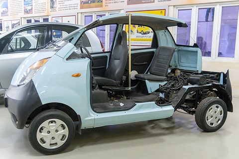 Pale blue small car with its body sides cut away, showing the seats, floor, rear engine and wiring. Opens a larger view