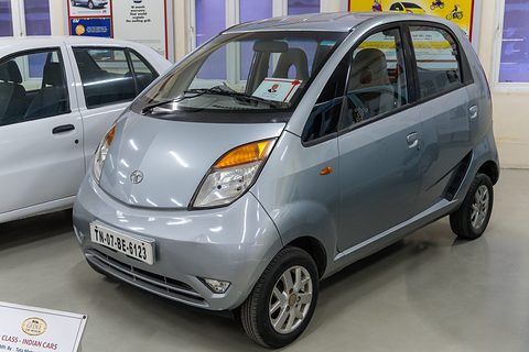 Silver small hatchback on a museum floor beside a white saloon, an information panel in front. Opens a larger view