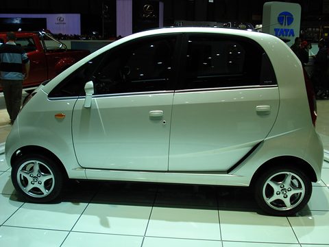 Side view of a pale green small hatchback with alloy wheels on a white show floor, a Tata sign behind. Opens a larger view