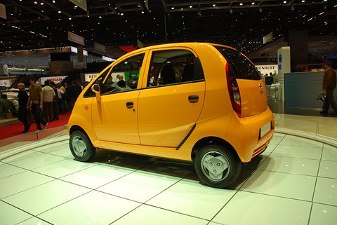 Rear of an orange small hatchback on a white turntable in a busy show hall, a Renault stand behind. Opens a larger view