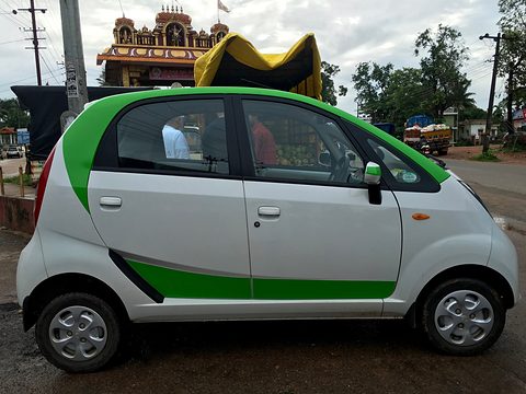 Side view of a white small hatchback with green decals on a road, a temple and trees behind. Opens a larger view
