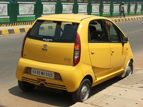 Rear of a bright yellow small hatchback parked by a green metro-works hoarding. Opens a larger view