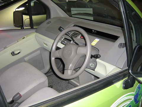 Grey two-spoke steering wheel, a pale grey dashboard with central display and grey cloth seats. Opens a larger view