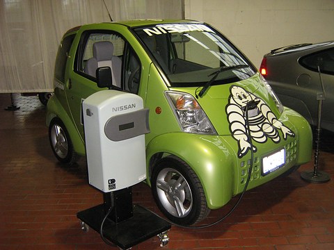 Lime-green small electric car with a Michelin Man on its bonnet beside a white Nissan charging stand.