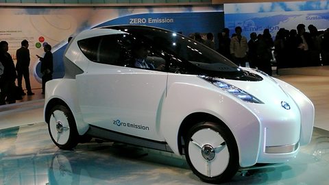 White narrow tandem two-seat concept with blue LED lamps and covered wheels on a show floor. Opens a larger view