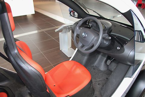 Red and black front seat with a rear seat behind, a steering wheel and dashboard pod, seen from the side. Opens a larger view