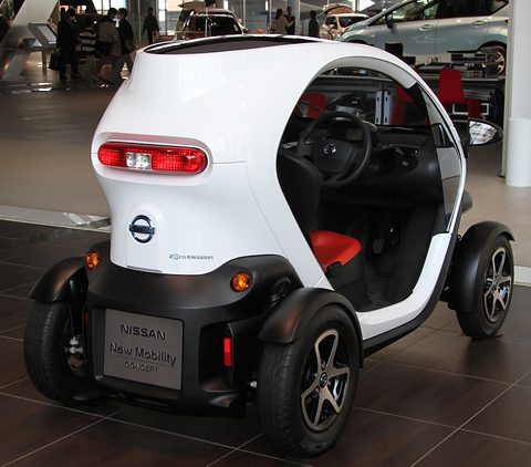 Rear of a white tandem two-seater with a Nissan badge and a New Mobility Concept plate on a dark floor. Opens a larger view
