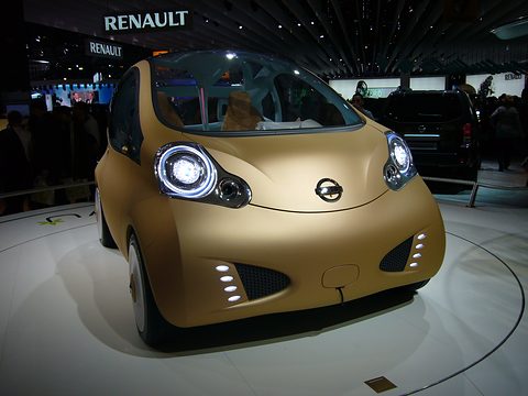 Matt gold rounded three-seat concept with round lamps on a white turntable, visitors in a dark hall behind. Opens a larger view