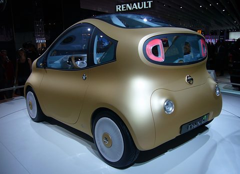 Rear of a matt gold rounded concept with a pink-rimmed rear window and white wheels on a turntable. Opens a larger view