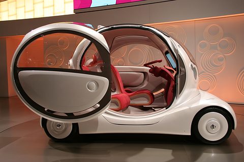 Side view of a white bubble concept with a large circular door swung wide and red seats inside. Opens a larger view