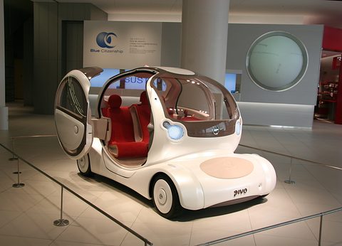 White bubble concept with round doors open and red seats inside, behind a rope on a gallery floor. Opens a larger view