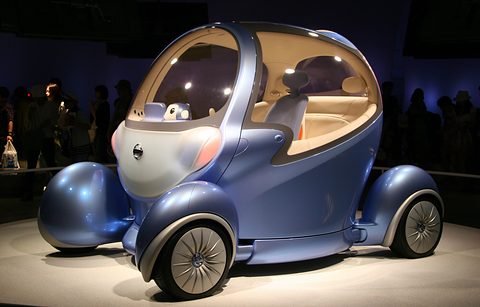Blue bubble-shaped concept with spoked wheels in separate pods under a spotlight on a dark stand. Opens a larger view