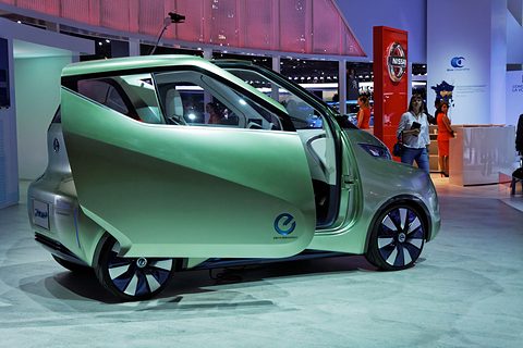 Pale green concept with a large door swung open on a show floor, visitors and a Nissan sign behind. Opens a larger view