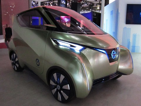 Pale gold three-seat concept with a sharp LED light bar and black-and-white wheels on a show floor. Opens a larger view