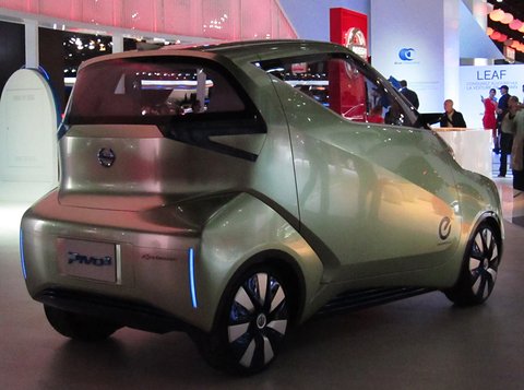 Rear of a pale gold tall concept with a Pivo3 badge and blue-lit wheels, show stands behind. Opens a larger view