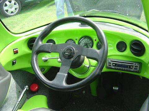 Lime-green moulded dashboard with round gauges, a Grant steering wheel, toggle switches and a car radio. Opens a larger view