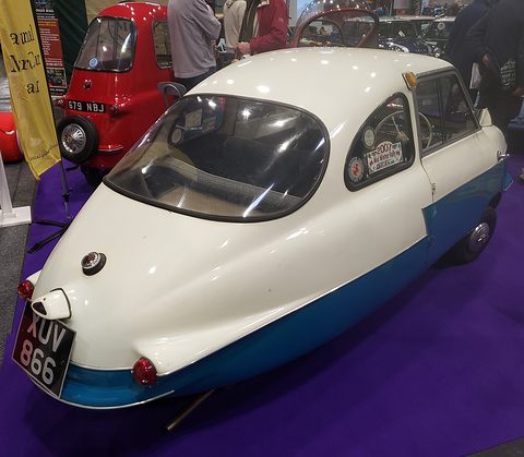 Narrow pointed tail of a white and blue microcar with registration XUV 866 on purple carpet. Opens a larger view