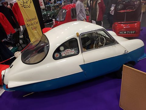 White and blue three-wheeler with a bubble rear window and tapering tail on purple carpet.