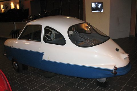 White and blue three-wheeler with a pointed tail and bubble rear window on a dark tiled floor. Opens a larger view