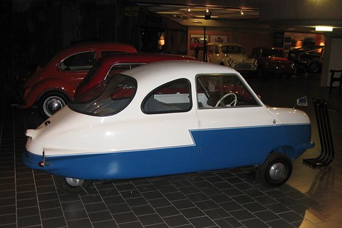 White over blue three-wheeler with bubble rear window, in a dark showroom.