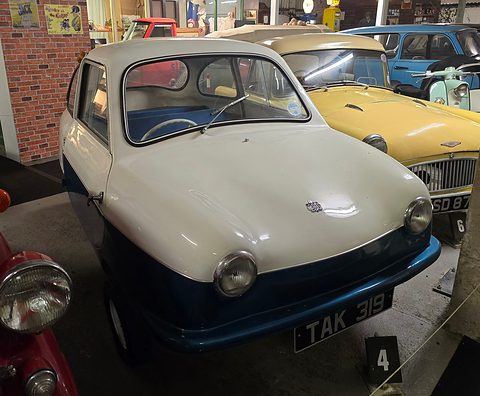 White and blue microcar with registration TAK 319 among other classic cars indoors. Opens a larger view