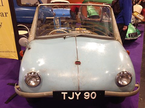 Pale blue rounded nose with two headlamps, chrome bumper and registration TJY 90 under a folding frame. Opens a larger view