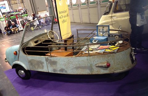 Long open pale blue body with chrome rails, steering wheel and a load bed of papers, on purple carpet.