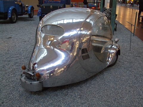 Rear quarter of a mirror-polished aluminium egg with louvres and a small oval rear window.