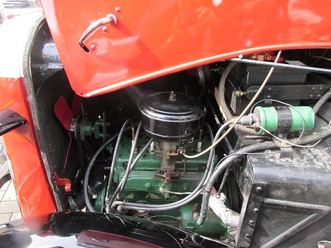 Green four-cylinder engine with a black air filter and red coil, under a raised red bonnet side. Opens a larger view