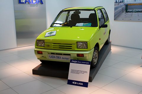 Front of a lime-green small hatchback on a black plinth, a Clean Air Forever sticker on the bonnet and a LADA placard in front. Opens a larger view