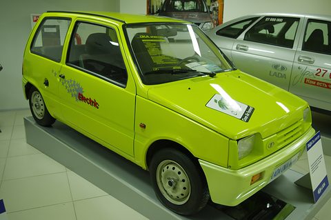 Lime-green small three-door hatchback with Electric graphics on its doors, on a museum floor beside a silver Lada.